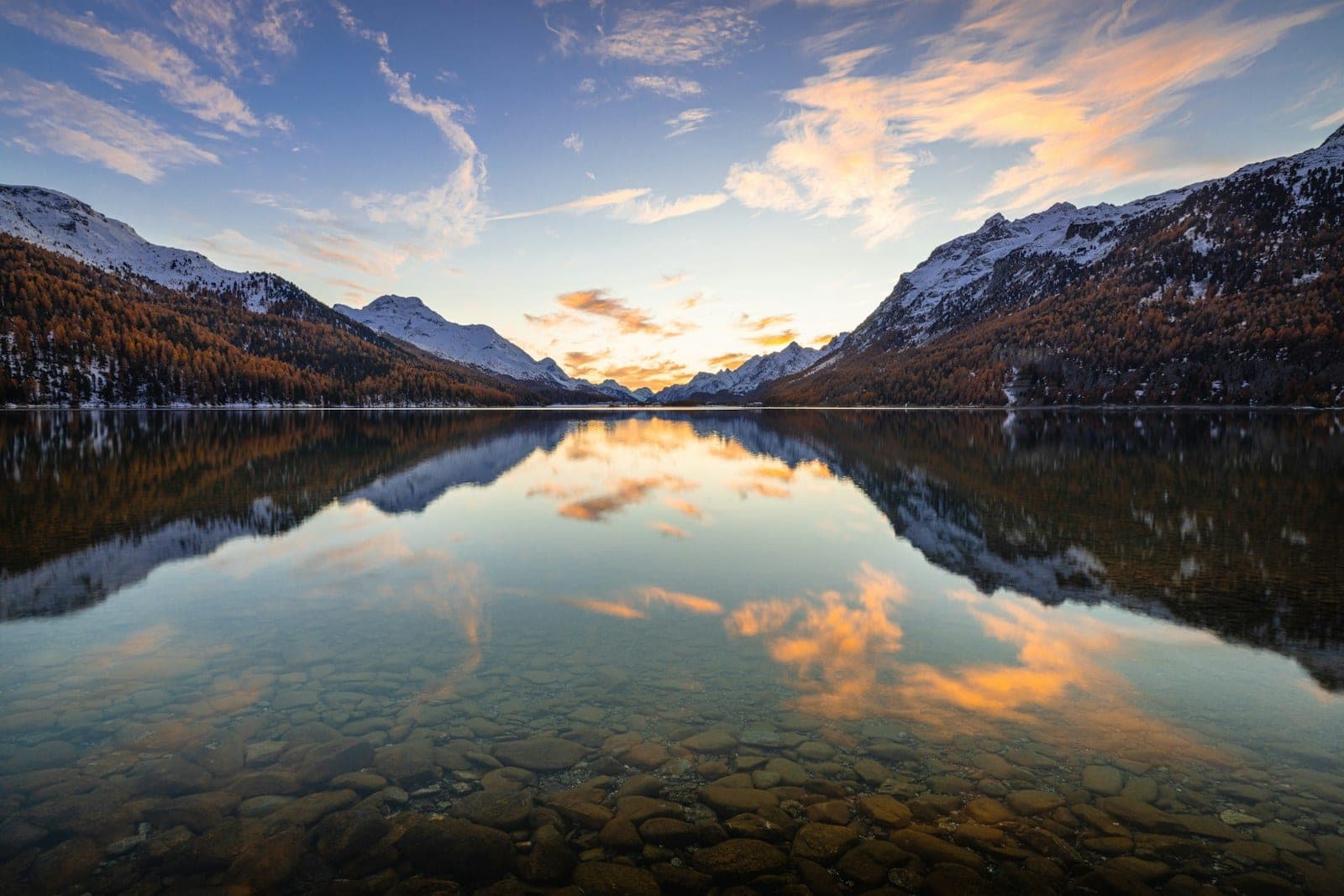 A still lake at sunset reflecting cloud and dark autumn ridges
