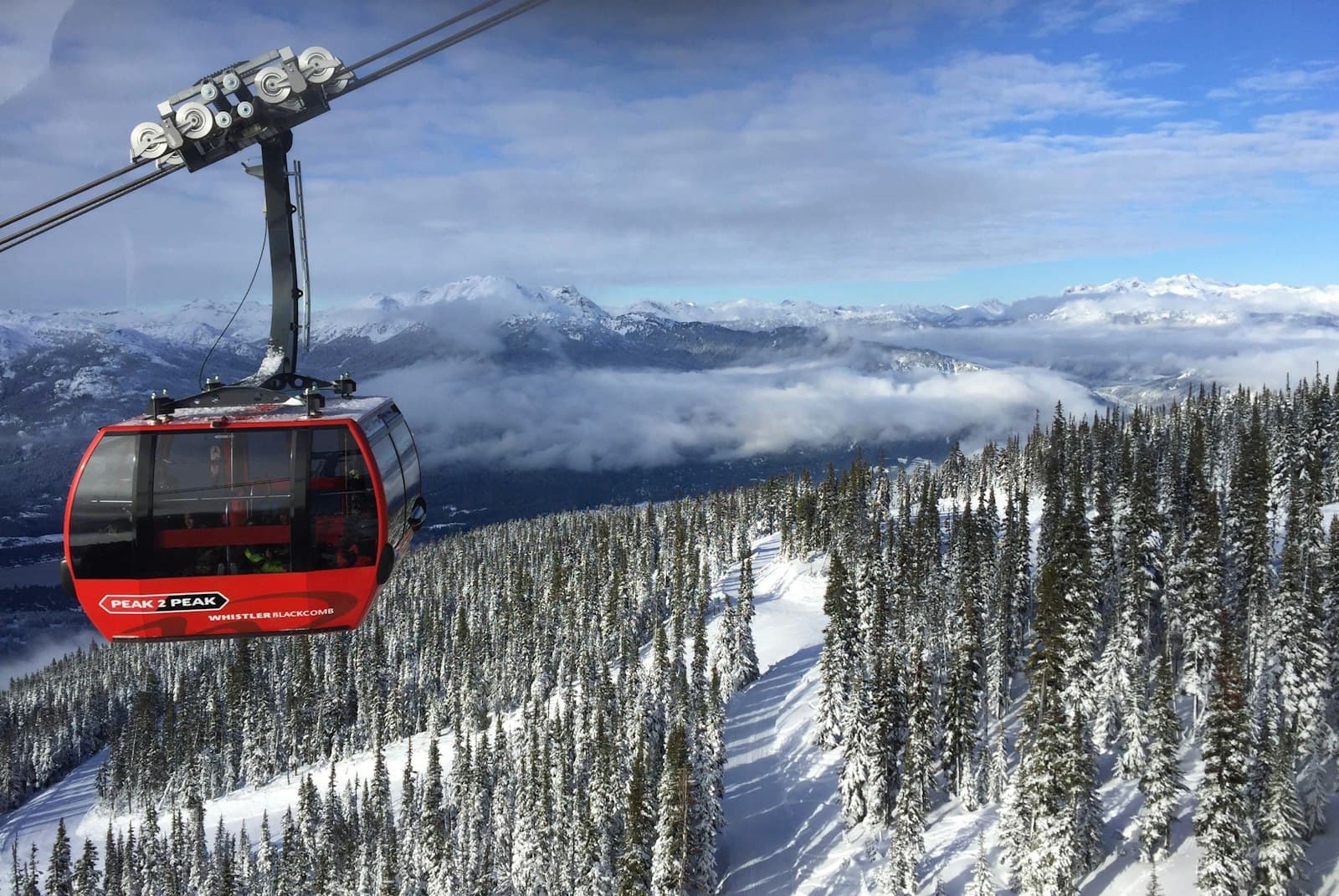 A red gondola cabin crossing above snow-covered evergreen forest