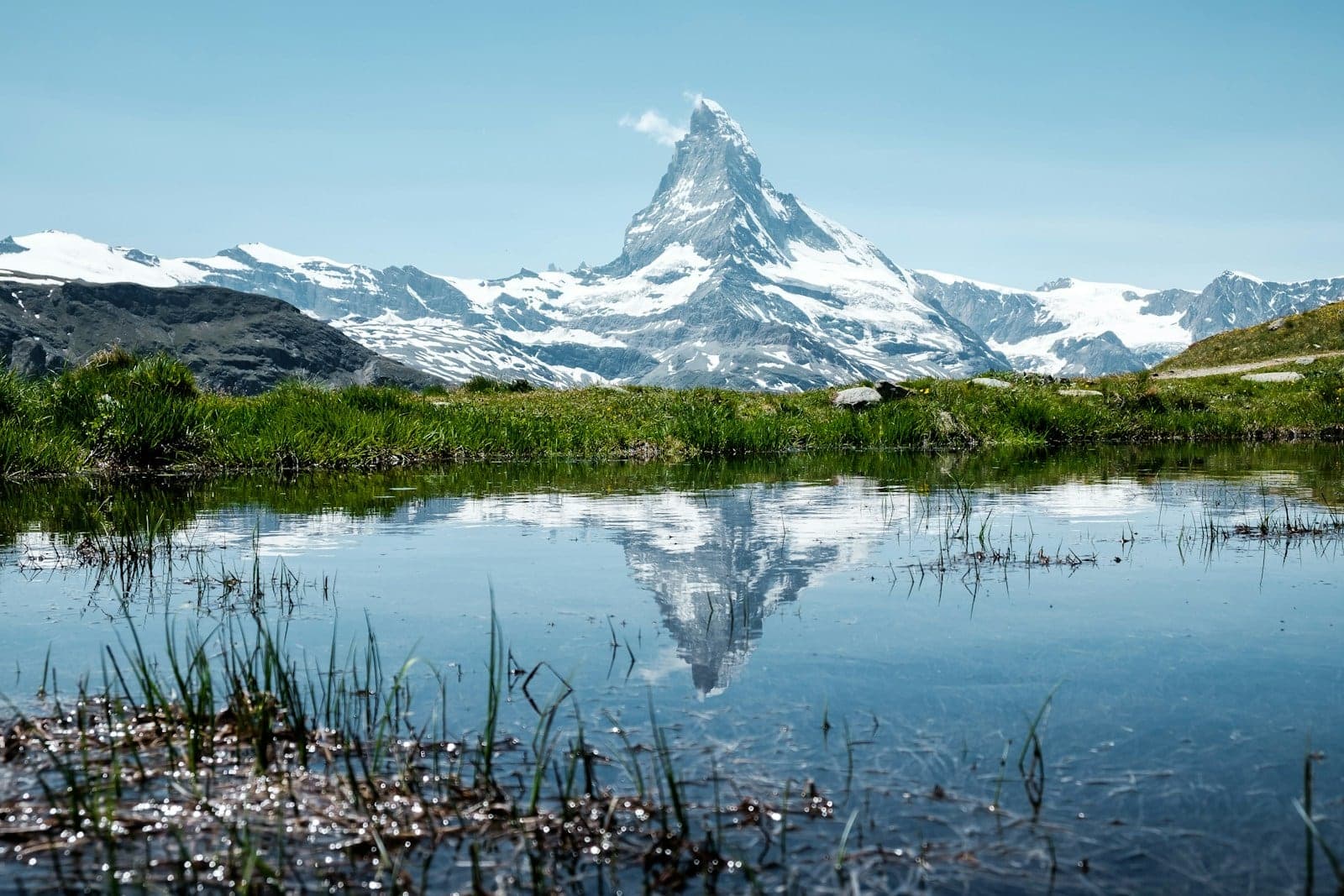 The Matterhorn mirrored in a still alpine tarn, grass at the water's edge